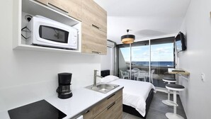 Habitación de hotel compacta con kitchenette, una cama, un pequeño comedor y vista al mar.