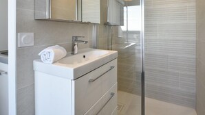 Un baño moderno con ducha de vidrio, tocador blanco con lavamanos y un espejo grande encima.