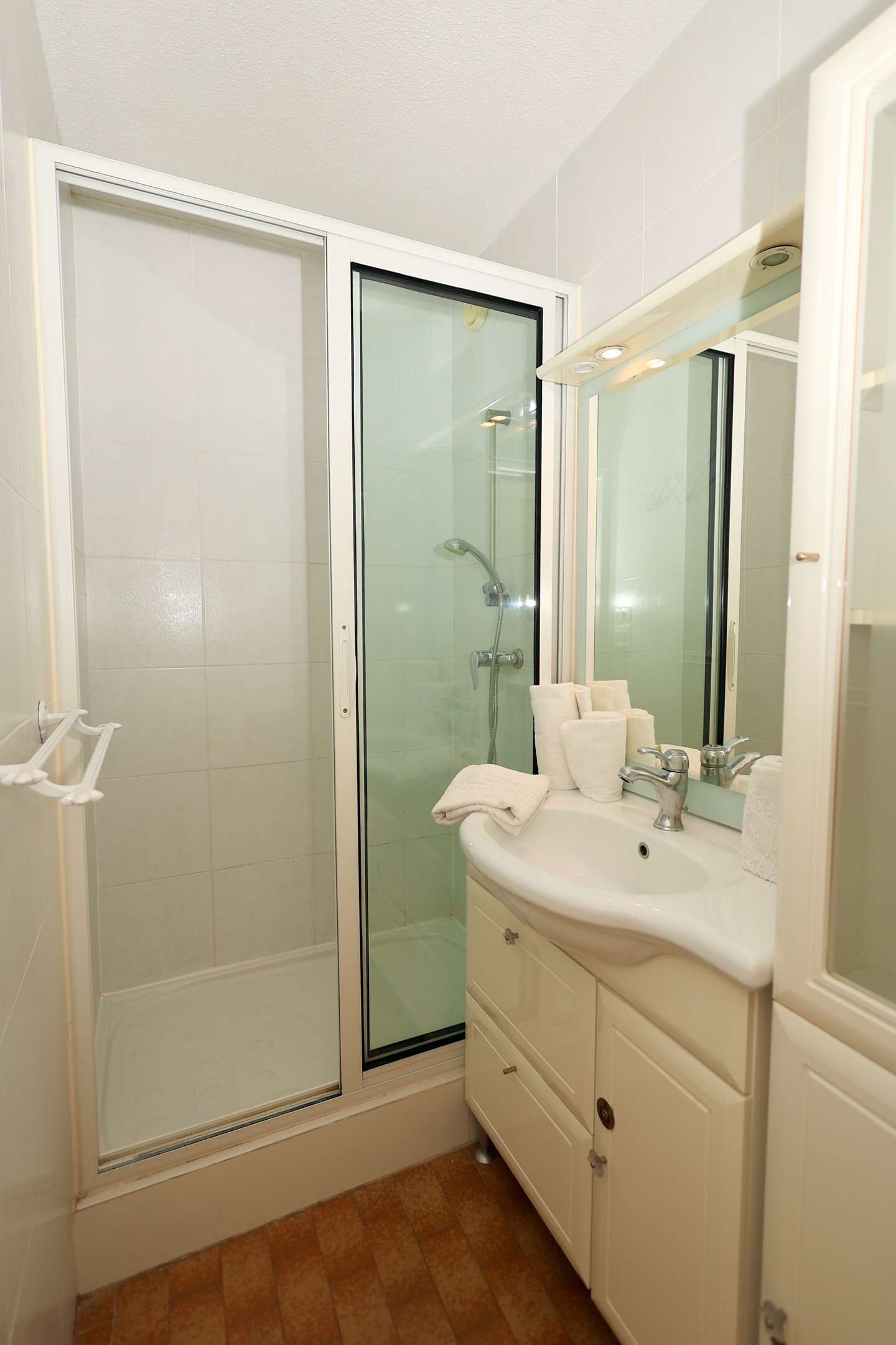 Ein Badezimmer mit einer Glaskabine zur Dusche, einem weißen Waschbecken inklusive Spiegel und Holzboden.