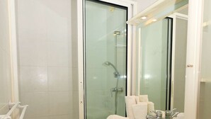 Un baño con ducha envuelta en vidrio, un lavamanos blanco con espejo y piso de madera.