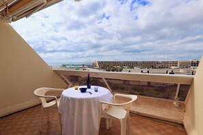 A balcony with a table and chairs, overlooking a coastal area with buildings in the background. - Studio Héliopolis AB419 - 2 people (AGDE)