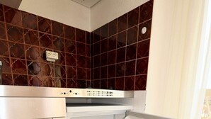 Una cocina con un refrigerador blanco, una encimera blanca y un salpicadero de azulejos marrones.