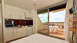 Un dormitorio con una cama grande, una kitchenette con microondas y un balcón con mesa y sillas.