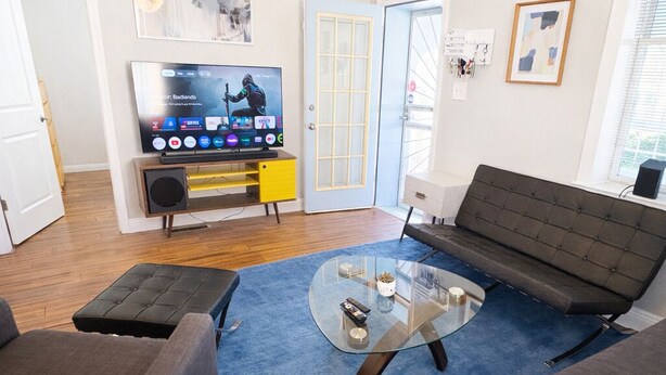 A living room with a sofa, ottoman, glass coffee table, and a TV.