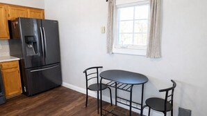 A kitchen with a black refrigerator, wooden cabinets, a window with curtains, and a dining table with chairs.