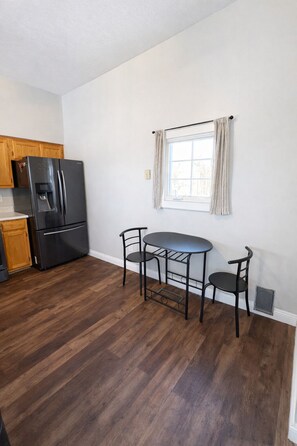 A kitchen with a black refrigerator, wooden cabinets, a window with curtains, and a dining table with chairs.