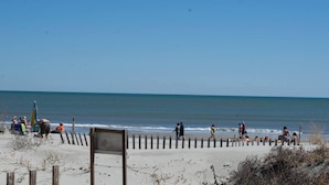 A beach with people walking along the shore, a wooden fence, and a clear blue sky. - Myrtle Beach Pelican's Watch Shore Drive Condo (Myrtle Beach)