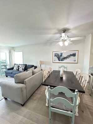 Ein Wohnzimmer mit einem dunklen Holzesstisch, weißen Stühlen, einem grauen Sofa und einem Deckenventilator.