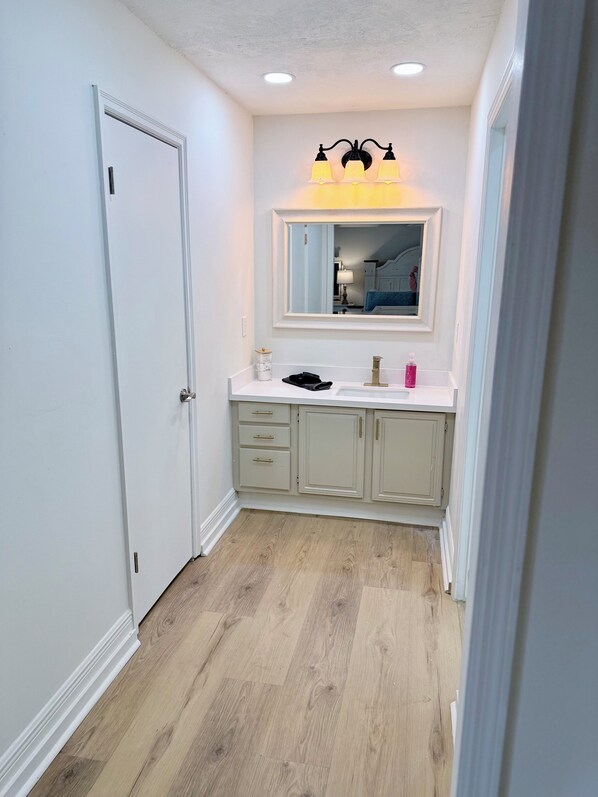 A narrow hallway with a white door, a vanity with a mirror, and a light fixture above it.