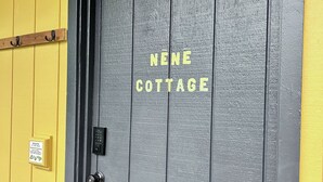A door with 'NENE COTTAGE' written on it, a keypad lock, a small welcome sign, and a light fixture above the door. - Nene Cottage on Pali'uli Estate by an active Volcano (Volcano)