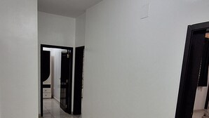 Ein Korridor mit weißen Wänden und Fliesenboden, der zu einem Raum mit einer schwarzen Tür führt.