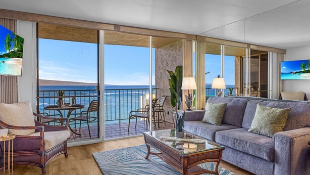 En rummelig opholdsstue med balkon med udsigt over havet, møbleret med sofa, lænestole og sofabord.