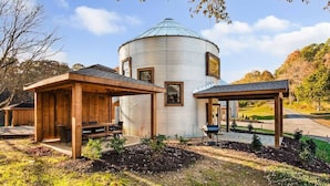Un chalet rustique doté d’un bâtiment principal de forme cylindrique, de structures en bois et d’un jardin bien entretenu.