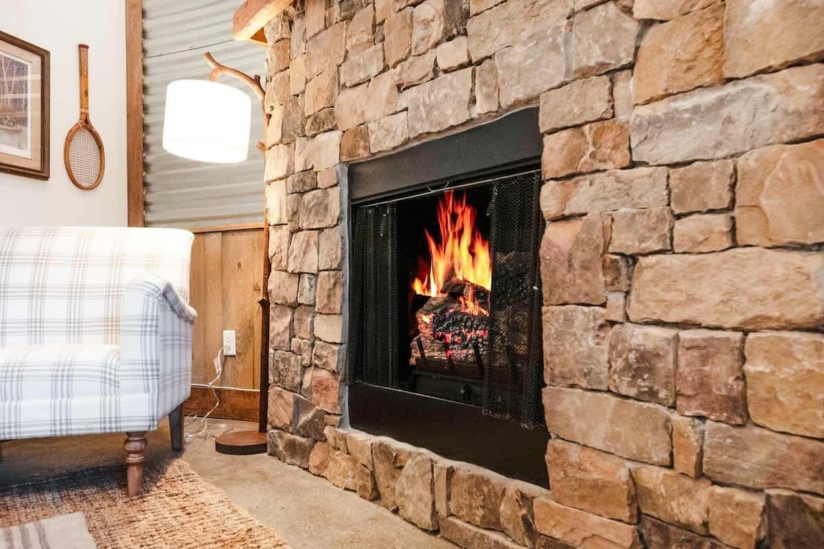 A stone fireplace with a fire, a plaid sofa, and a tennis racket on the wall.