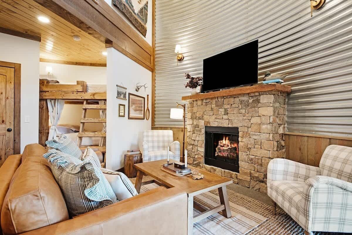 A cozy living room with a stone fireplace, a flat-screen TV mounted above it, and a wooden ceiling.