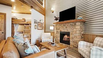 A cozy living room with a stone fireplace, a flat-screen TV mounted above it, and a wooden ceiling.