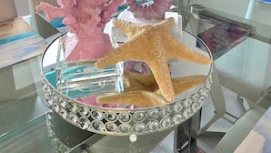Un tavolo di vetro con un centrotavola decorativo a tema marino, con un cavalluccio marino e coralli, una sedia e un quadro appeso alla parete.
