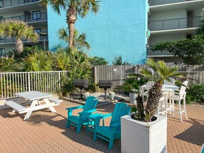 An outdoor patio area with turquoise chairs, a white table, and a potted palm tree. - Modern Beachfront Studio - Ocean View - Free Beach Chairs (Panama City Beach)