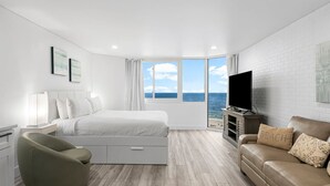 A modern bedroom with a large bed, a TV, a sofa, and a view of the sea. - Modern Beachfront Studio - Ocean View - Free Beach Chairs (Panama City Beach)