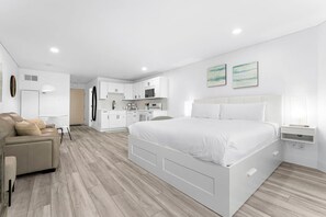 A modern hotel room with a large bed, a sofa, a kitchen area, and a dining table. - Modern Beachfront Studio - Ocean View - Free Beach Chairs (Panama City Beach)