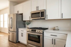 Une cuisine moderne dotée d’appareils électroménagers en acier inoxydable, de meubles de rangement blancs et d’une cuisinière à gaz.