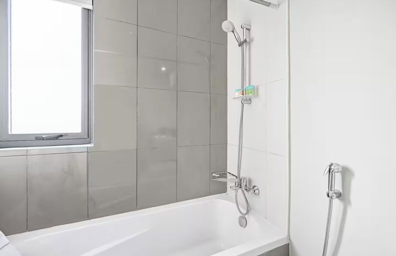 Une salle de bain moderne avec une baignoire blanche, une douche équipée d’un pommeau de douche à main et une fenêtre laissant entrer la lumière naturelle.