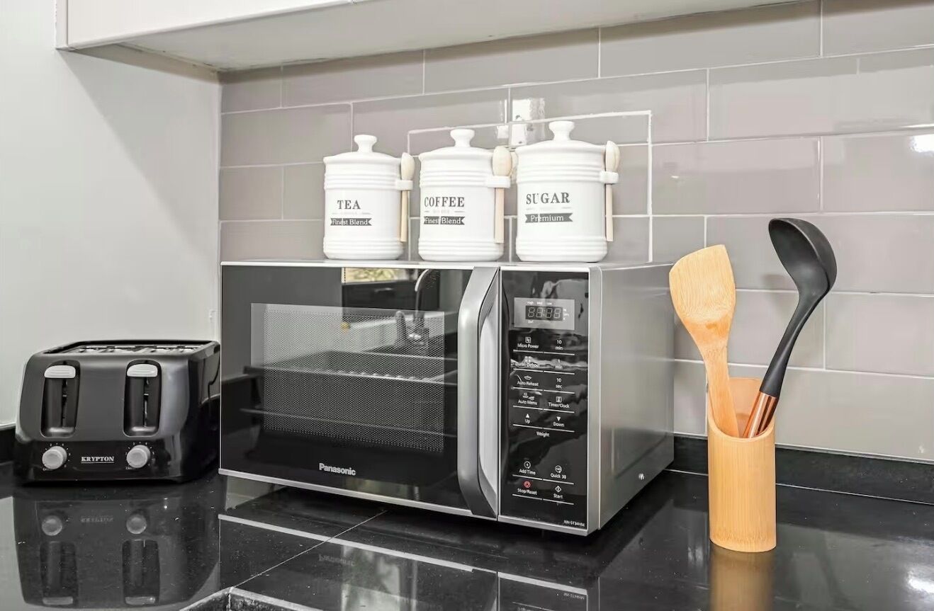A kitchen with a toaster, a microwave, and three white containers labeled tea, coffee, and sugar.