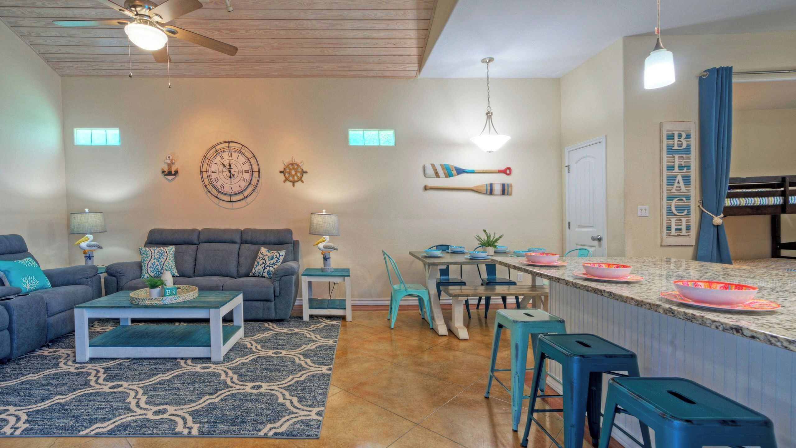 Una sala de estar con sofá, mesa de centro y sillas, un comedor con mesa y sillas, y una cocina con mostrador y taburetes.