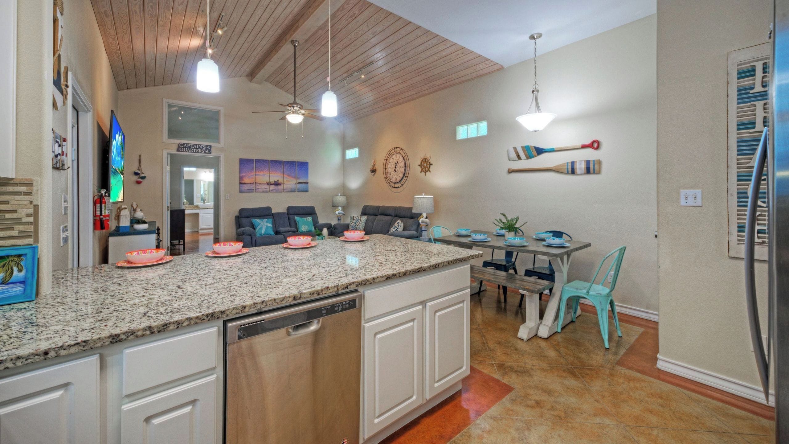 A kitchen with granite countertops, white cabinetry, a dining area with a table and chairs, and a ceiling fan.