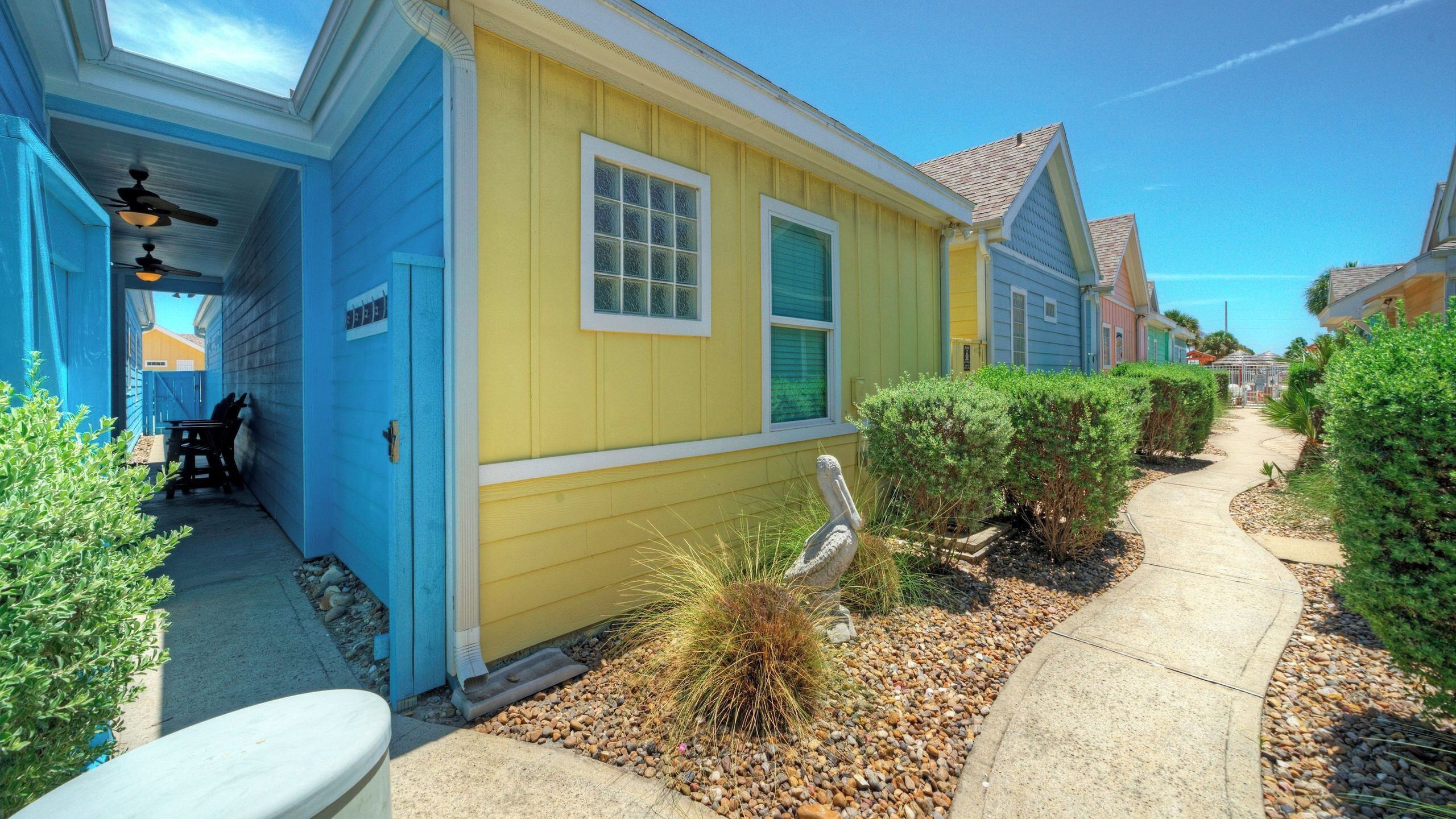 A row of colorful houses with a pathway, a pelican statue, and a clear sky.
