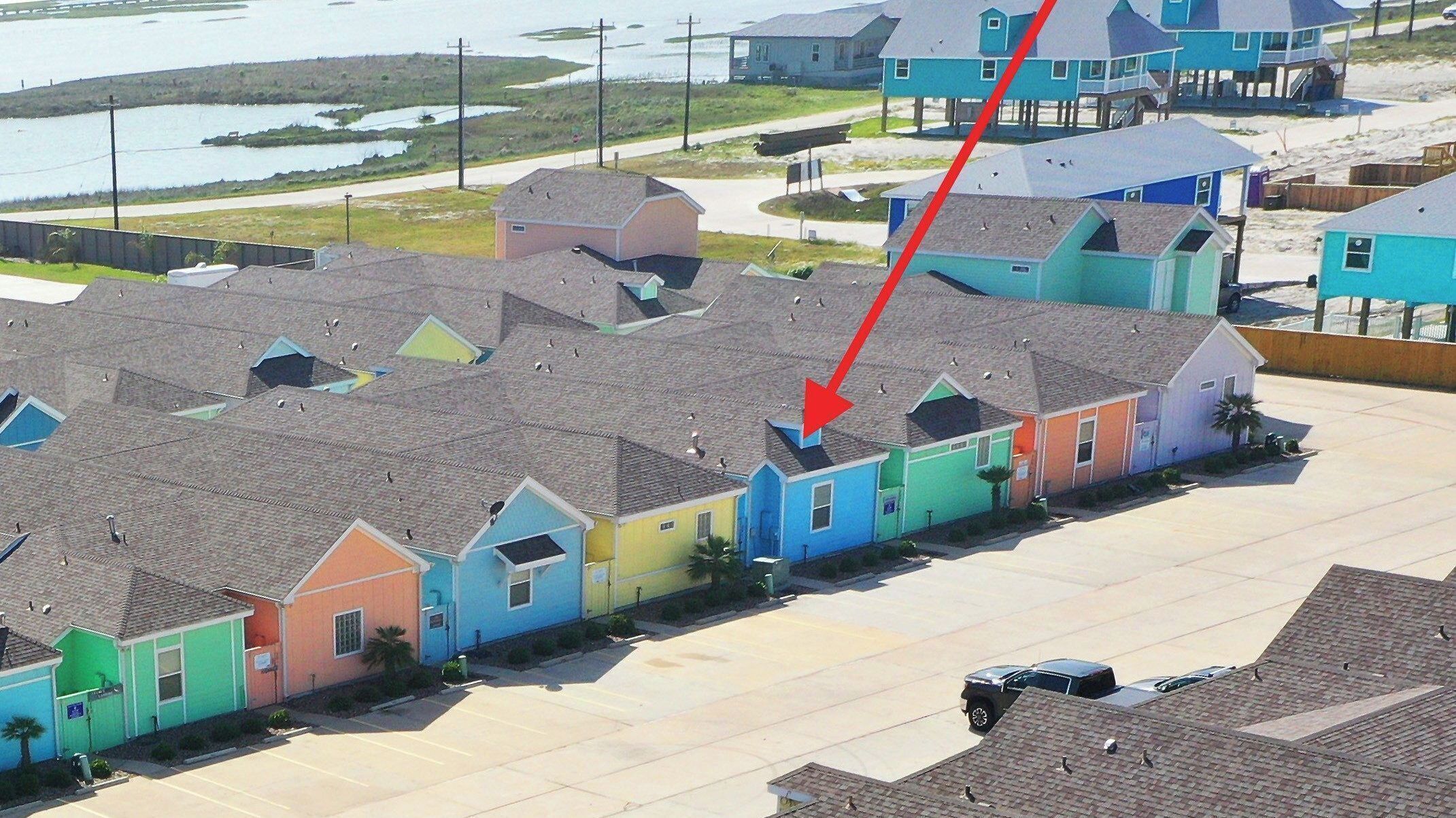 Un quartier résidentiel avec des maisons aux couleurs vives, un parking et une étendue d’eau en arrière-plan.
