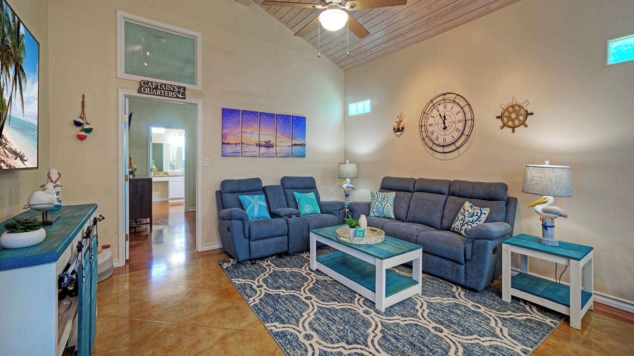 A living room with a blue sofa set, a coffee table, a wall clock, and a ceiling fan.