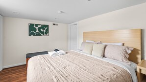 Ein Schlafzimmer mit einem hölzernen Kopfteil, einem Bett mit beigefarbener Bettwäsche, einer Bank und einem grünen, abstrakten Gemälde an der Wand.