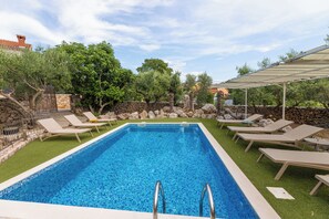 Une piscine rectangulaire bordée de carreaux, entourée de chaises longues et d’un mur en pierre.