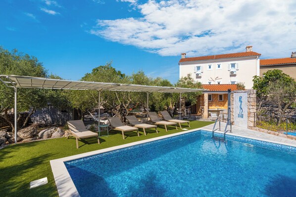 Une piscine avec des chaises longues, une pergola et un mur en pierre orné d’une mosaïque.