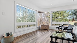 Una habitación con amplias ventanas, suelo de madera, un banco y una pequeña mesa.