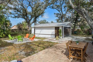 Un petit bâtiment d’un seul étage, doté d’un garage, entouré d’arbres et comprenant une terrasse avec des meubles d’extérieur.