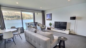 A modern living room with a sofa, TV, and dining area. - Amazing 2 Bedroom Lakeside Apartment (Queenstown)
