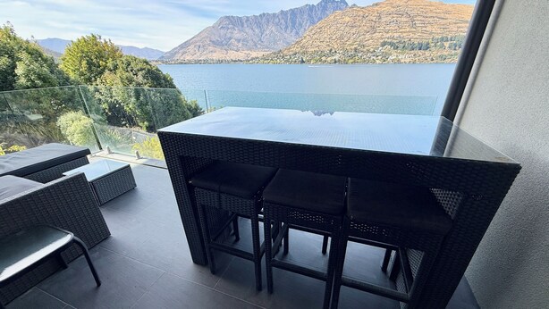 A balcony with a table and chairs, overlooking a lake and mountains. - Amazing 2 Bedroom Lakeside Apartment (Queenstown)