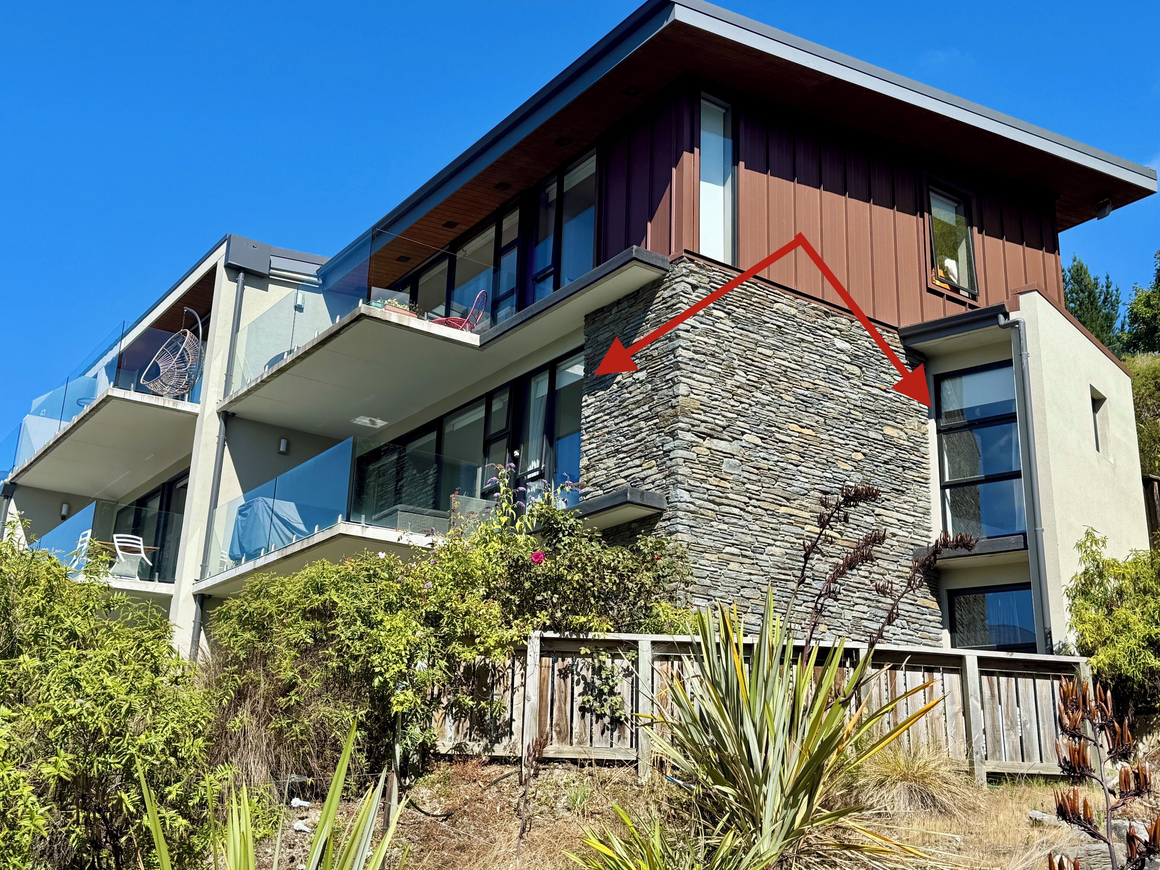 Une maison moderne à deux étages, dotée d’une façade en pierre, de balcons et d’une terrasse en bois.
