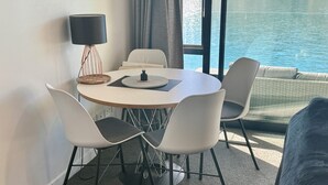A modern dining area with a round table, four chairs, a lamp, and a view of the water. - Amazing 2 Bedroom Lakeside Apartment (Queenstown)
