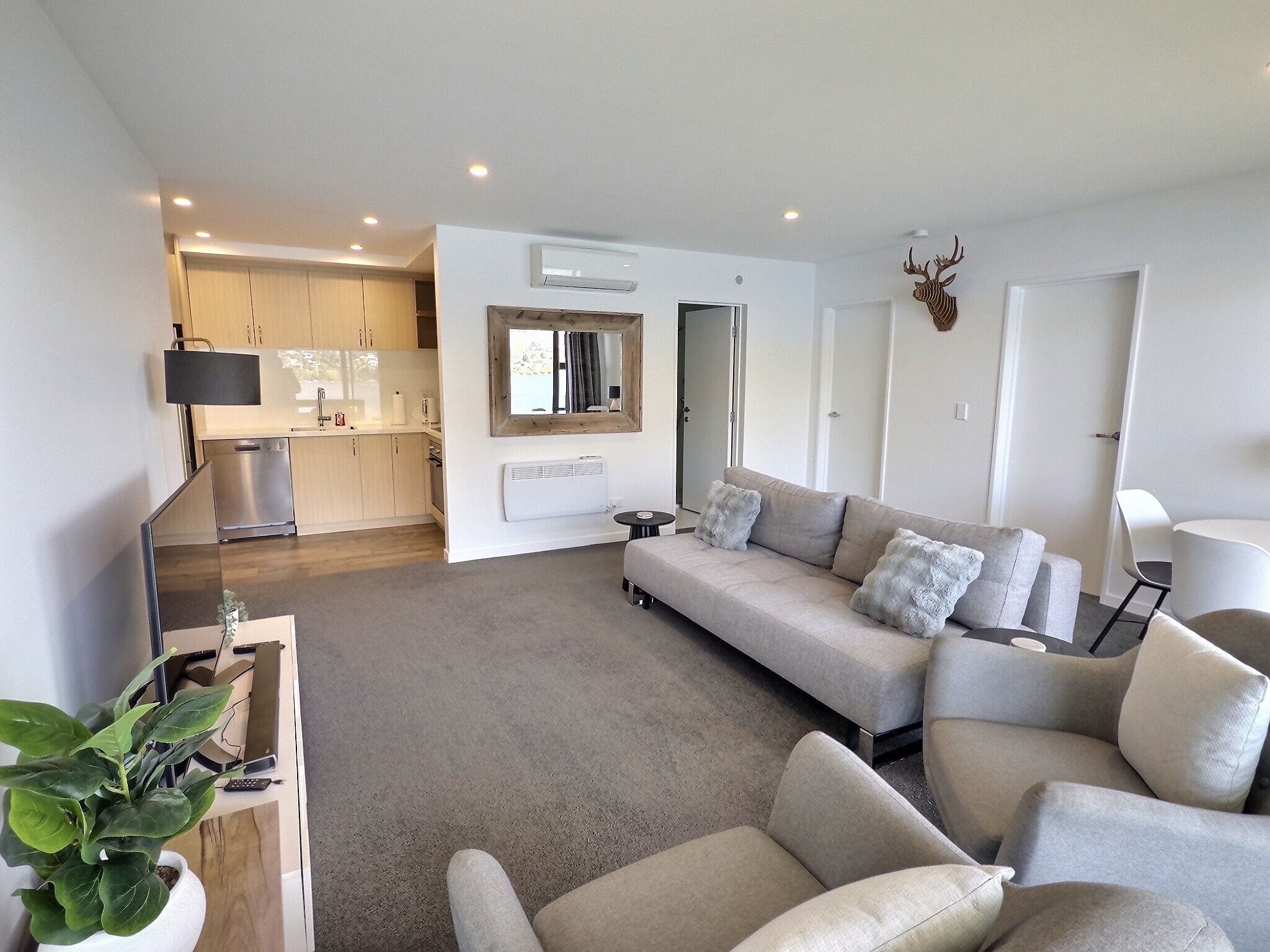 A modern living room with a sofa, a dining area with a table and chairs, and a kitchen with cabinets and appliances.
