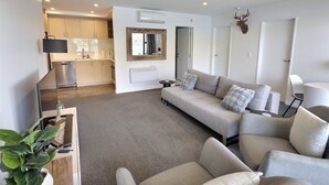A modern living room with a sofa, a dining area with a table and chairs, and a kitchen with cabinets and appliances. - Amazing 2 Bedroom Lakeside Apartment (Queenstown)