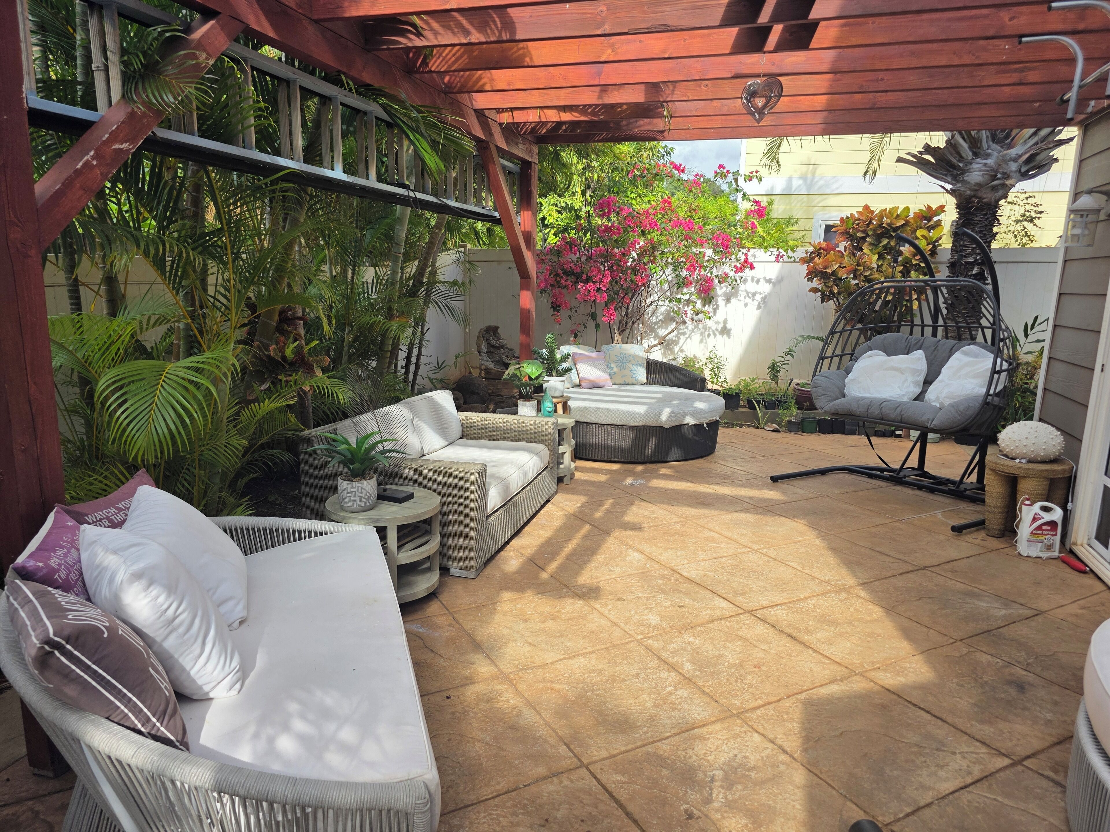Ein überdachter Patio-Bereich mit Korbmöbeln, einer runden Sitzecke und einem Hängestuhl.