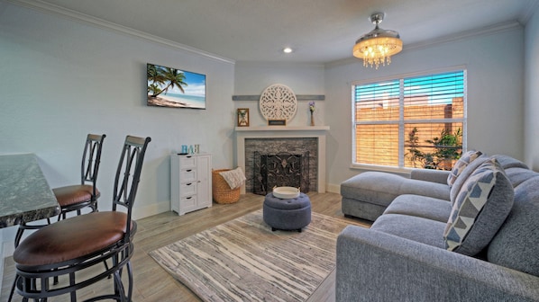 A living room with a fireplace, a dining area with chairs, a sofa, and a large window with blinds. - Seaside Haven by Avantstay Beautiful Condo + Communal Pool + Near North Padre Island and Whitecap Beach (Corpus Christi)