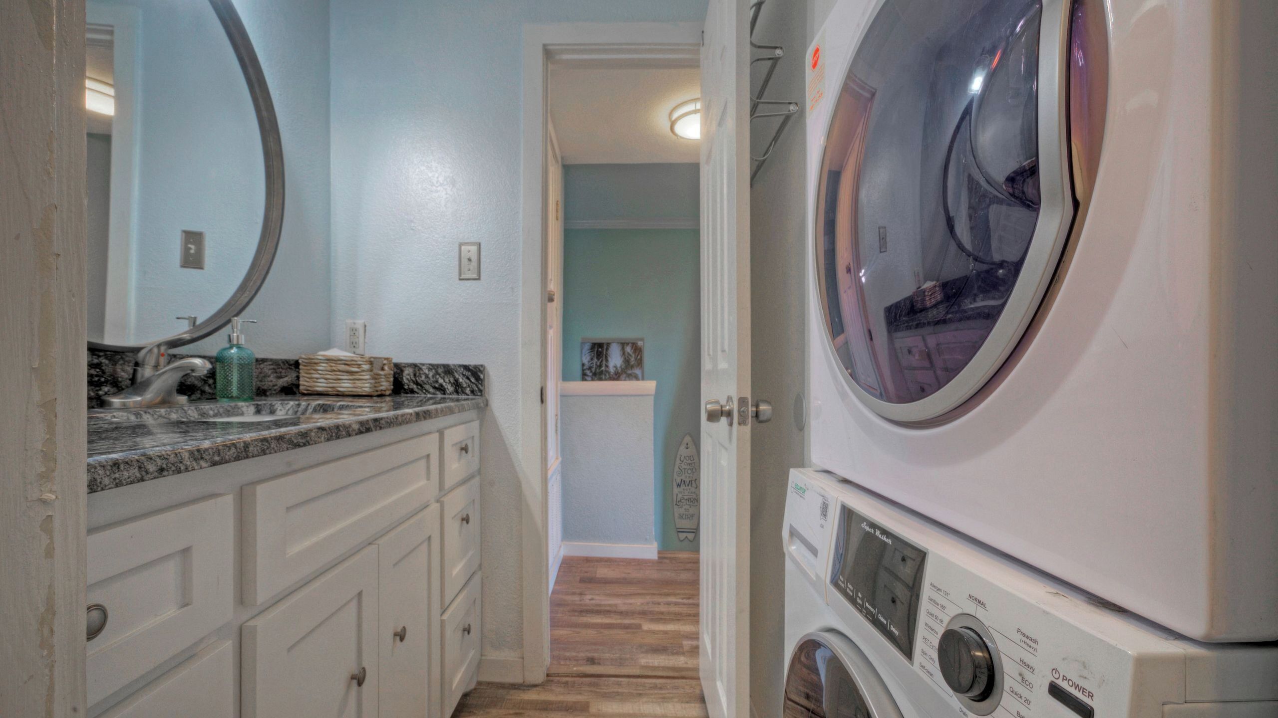 Une buanderie équipée d’un lave-linge, d’un évier avec un plan de travail en marbre et d’un miroir.