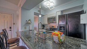 A kitchen with granite countertops, a stainless steel sink, a refrigerator, and a microwave.