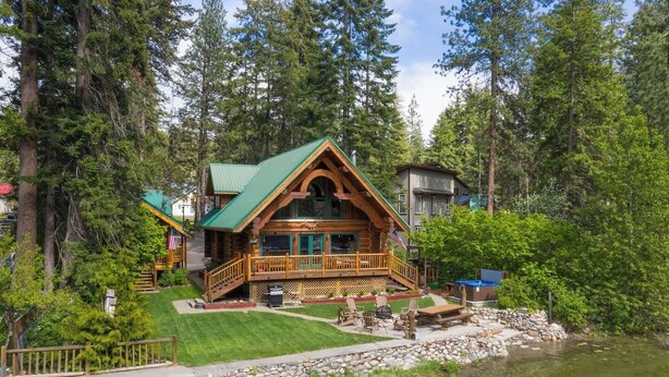 A log cabin with a green roof, a deck, and a stone-lined pond. - Riverfront Log cabin, sleeps 6 guests with hot tub (Leavenworth)