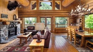 A log cabin interior with a stone fireplace, leather sofa, wooden dining table, and a mounted moose head. - Riverfront Log cabin, sleeps 6 guests with hot tub (Leavenworth)