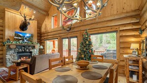 A log cabin interior with a fireplace, a Christmas tree, a dining table with placemats, and a mounted moose head. - Riverfront Log cabin, sleeps 6 guests with hot tub (Leavenworth)